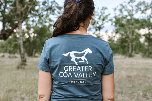 A person in a green landscape from behind in a petrol colored t-shirt with the imprint "Greater Côa Valley Portugal".