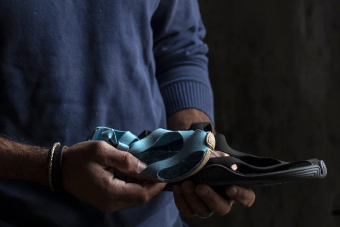 Close up of person in dark blue sweater holding two Wildling Shoes sandals in different colors at belly level.