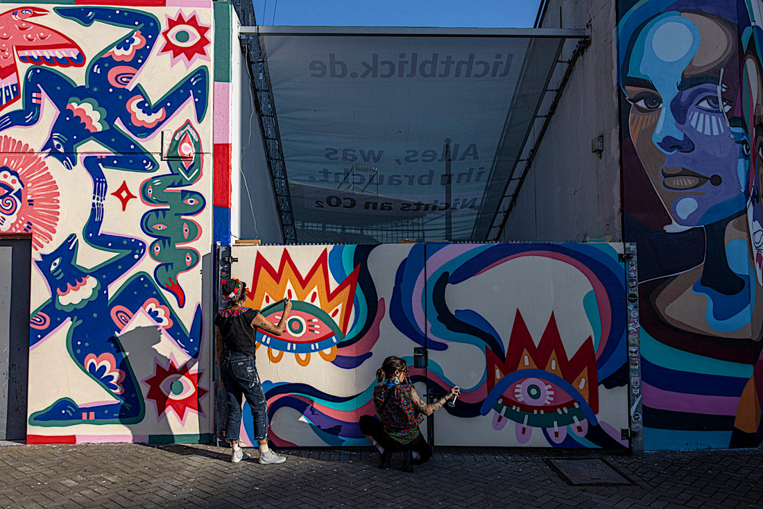The wall mural painted by Jumu Monster and Mari Pavanelli; in front of it, the two artists.