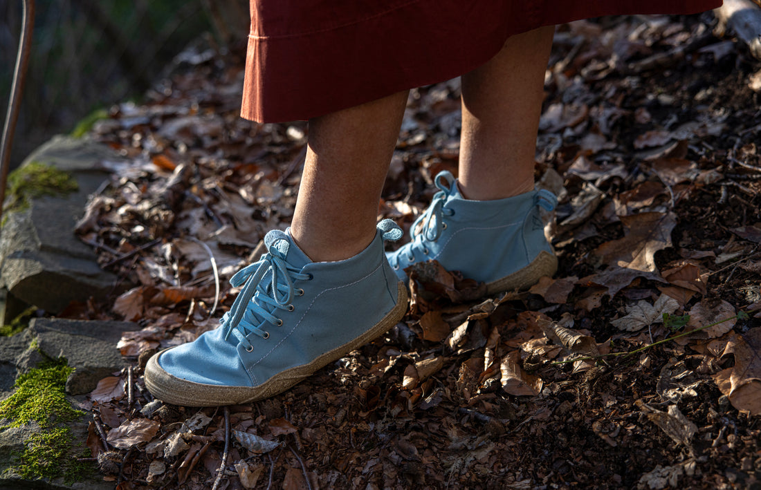 Close-up: two feet standing in Wildling shoes on a leaf-covered surface.
