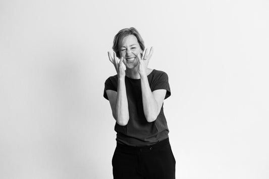 A black and white picture of Wildling Shoes founder and CEO Anna Yona. She is in the picture from head to waist, wearing a dark T-shirt and dark trousers, her gestures and facial expressions signaling agitation.