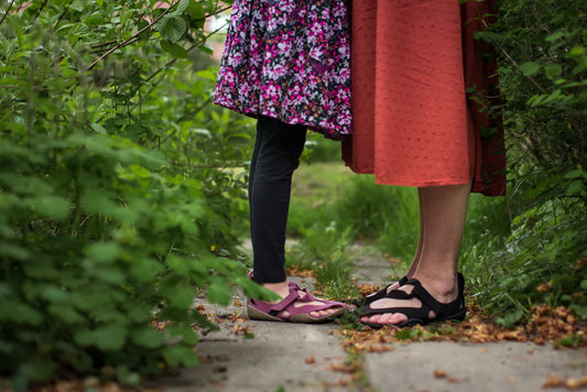 Two people up to about the waist. They stand on a narrow path between bushes, wearing colored skirts and Wildling barefoot shoes.
