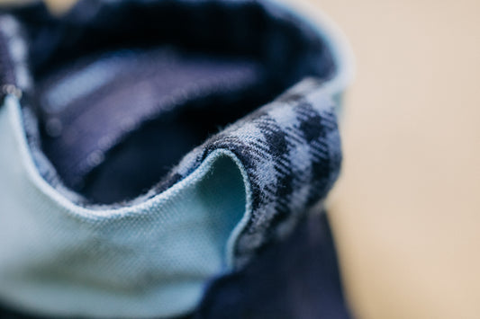 Detail view of the back of the minimal shoe Renette from diagonal above. You can see light blue and dark blue fabric elements and a light-dark plaid heel loop. 