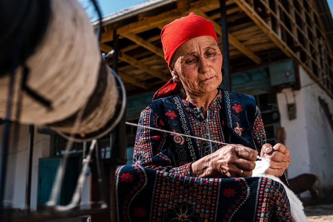 Cotton: fabric for arguing. A person wearing a bright red headscarf is deeply focused on spinning cotton by hand.